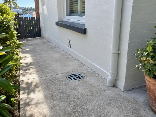 Outdoor concrete courtyard with a drain grate beside a painted house wall in Double Bay
